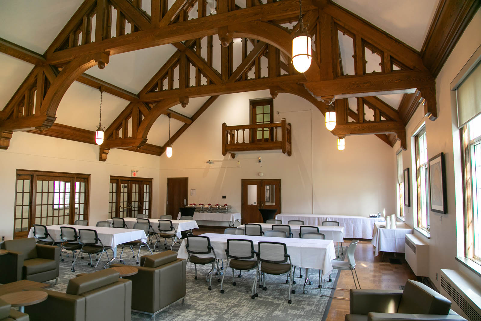A room with high vaulted ceilings and decorative wooden embellishments setup for a conference with 4 tables and mixed seating for 30 people