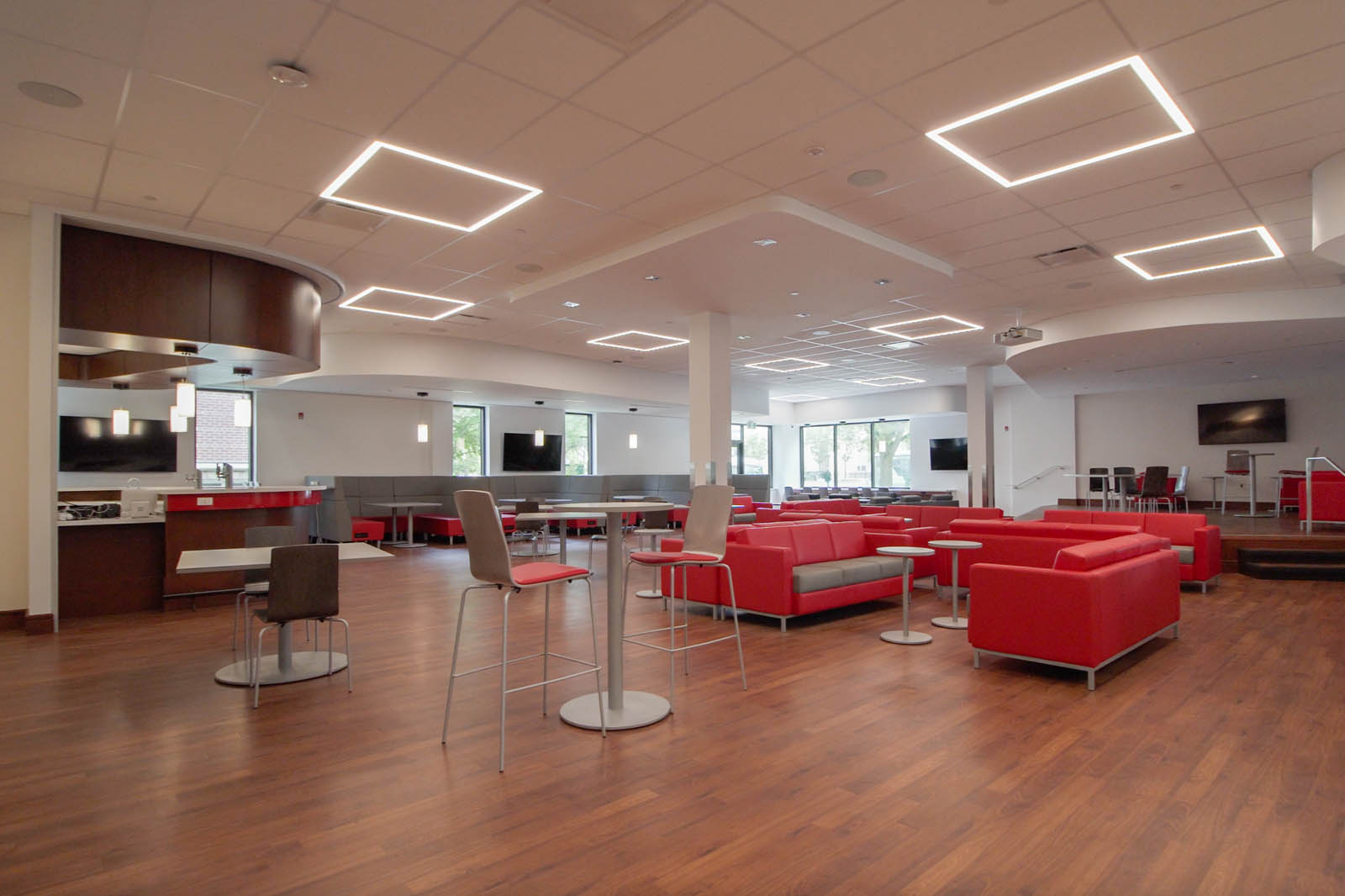 Modern student commons area with a bar, booths, tables, lounge seating and a small corner stage